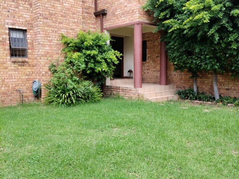 A rear view of a face brick house featuring a covered entrance with structural columns, tiled steps, and a well-maintained lawn area.