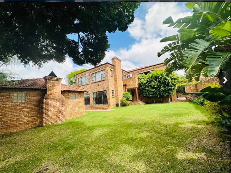 A spacious rear garden view featuring a multi-story brick house with a tiled roof, chimney, and established lawn area.
