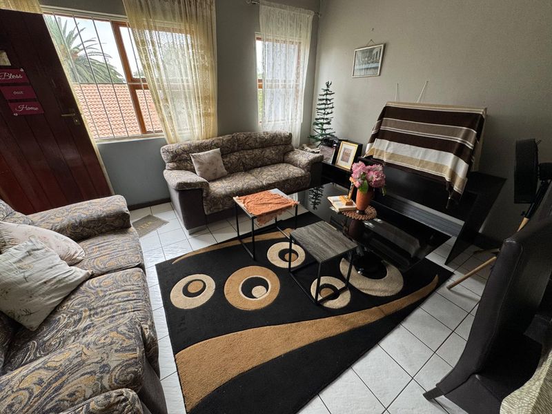 A living room featuring tiled flooring and large windows with security bars, providing natural light to the space.
