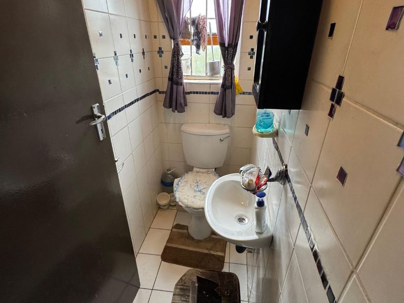 Compact bathroom featuring a wall-mounted basin, toilet, and tiled finishes. The space would benefit from cosmetic updates to modernize the dated tile work.