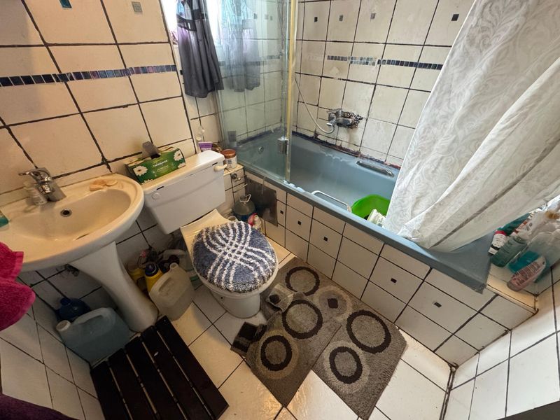 A dated bathroom featuring a pedestal basin, toilet, and a bathtub with a shower screen, requiring significant renovation and tile repair.