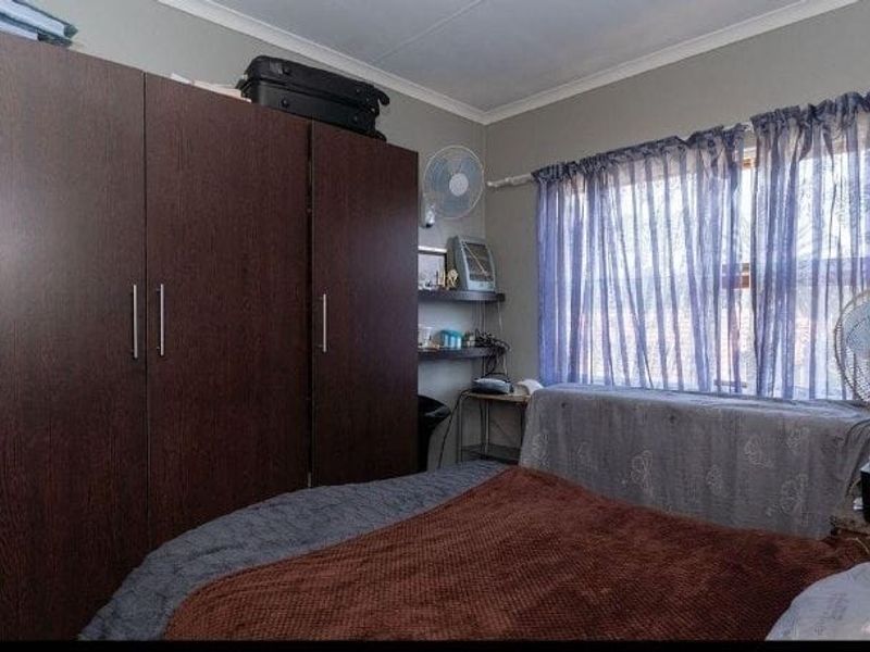 A bedroom featuring a large built-in wardrobe and window with curtains, providing functional storage and natural light.
