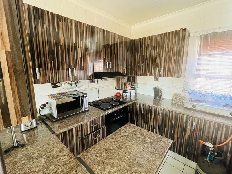 A functional kitchen featuring wood-grain laminate cabinetry, granite-look countertops, a built-in oven, and an electric hob with an extractor fan.
