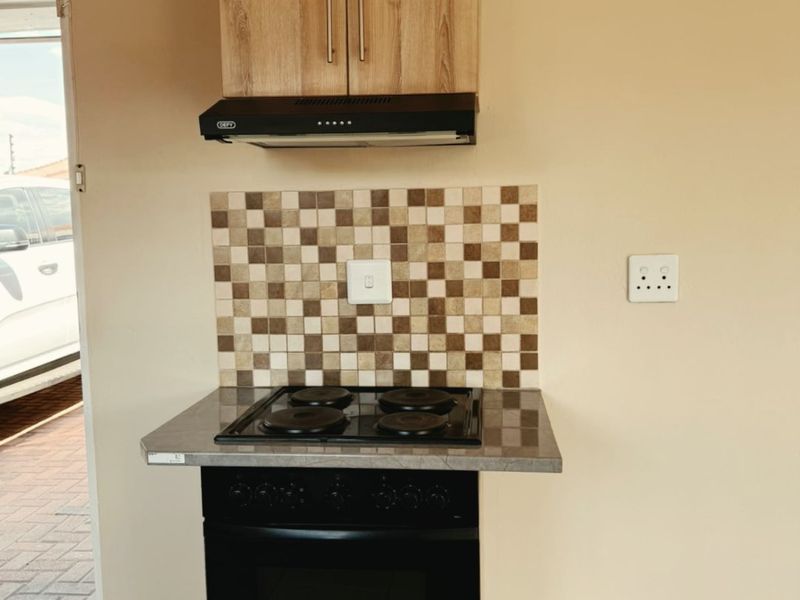 A compact kitchen area featuring a built-in oven, electric hob, extractor fan, and tiled backsplash with neutral cabinetry.