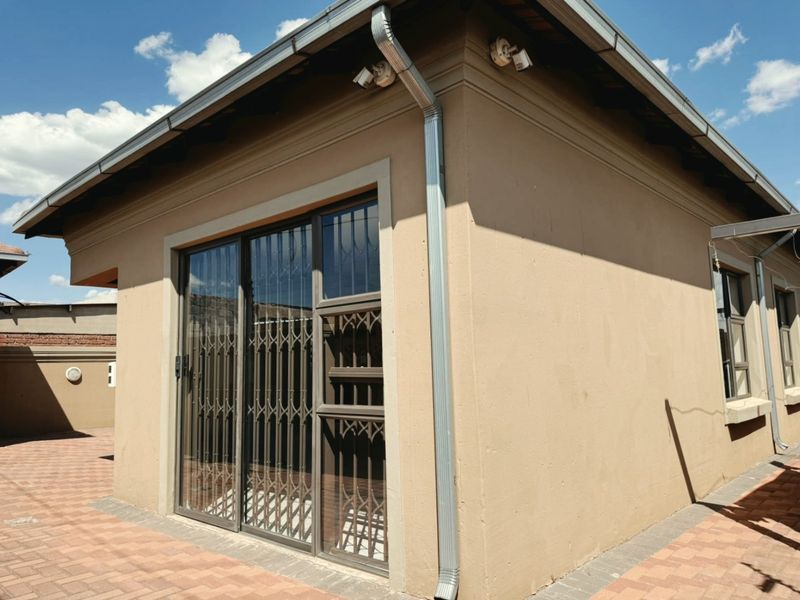 Rear exterior view of the property featuring a paved patio area, sliding glass doors with security gates, and functional downpipe drainage.