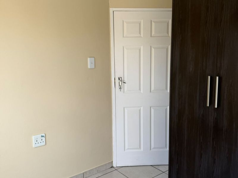 A clean, empty bedroom featuring neutral wall paint, tiled flooring, and a dark wood built-in wardrobe with modern handles.