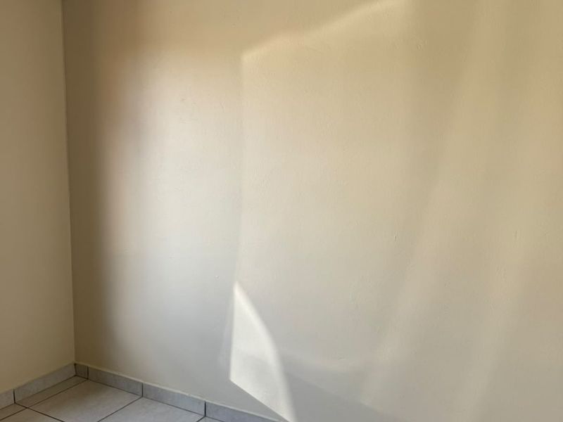 An empty bedroom featuring neutral painted walls, tiled flooring, and a security sensor, providing a blank canvas for personalization.