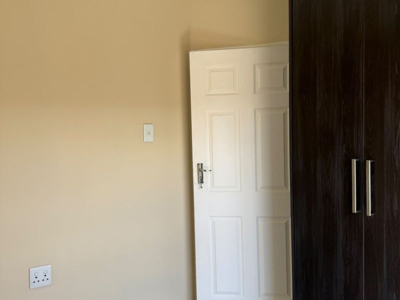 A clean, empty bedroom featuring neutral walls, tiled flooring, and a dark wood built-in wardrobe.