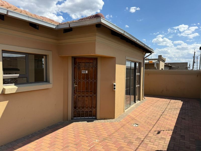 A rear exterior view featuring a paved patio area, secure entrance with a security gate, and sliding glass doors leading into the home.