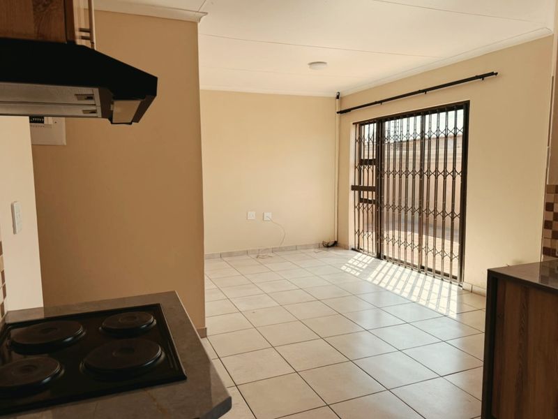 An open-plan living and kitchen area featuring tiled flooring, a built-in hob with extractor fan, and a sliding door leading to an outdoor space.