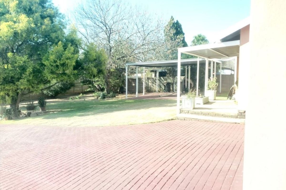 Rear garden area featuring a paved patio, covered carport structure, and established lawn with boundary fencing.