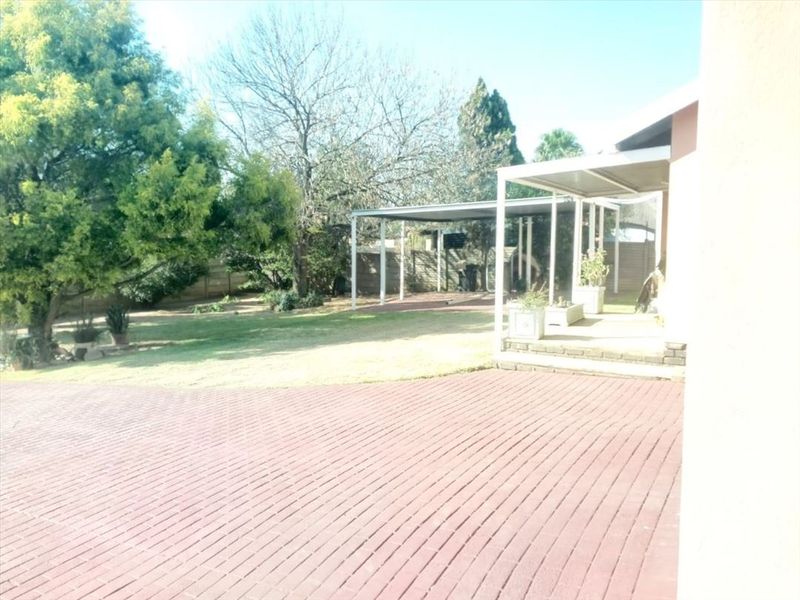 Rear garden area featuring a paved patio, covered carport structure, and established lawn with boundary fencing.