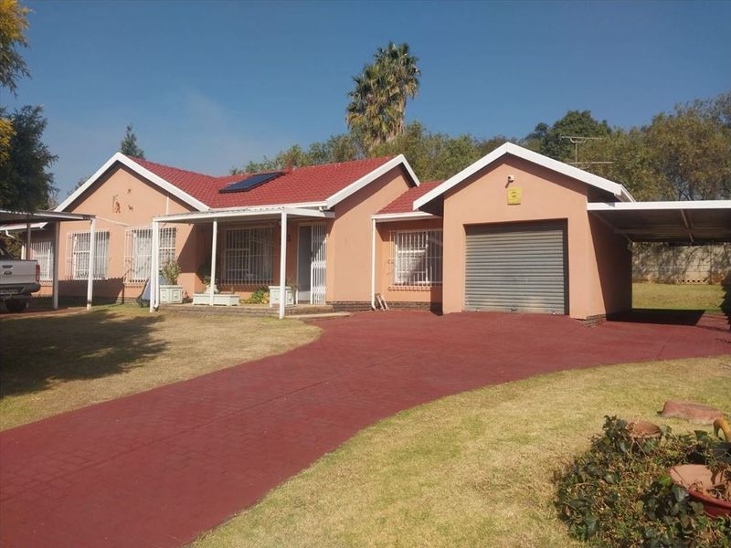 Front view of a single-story house featuring a tiled roof, solar water heater, attached garage, carport, and a paved driveway.
