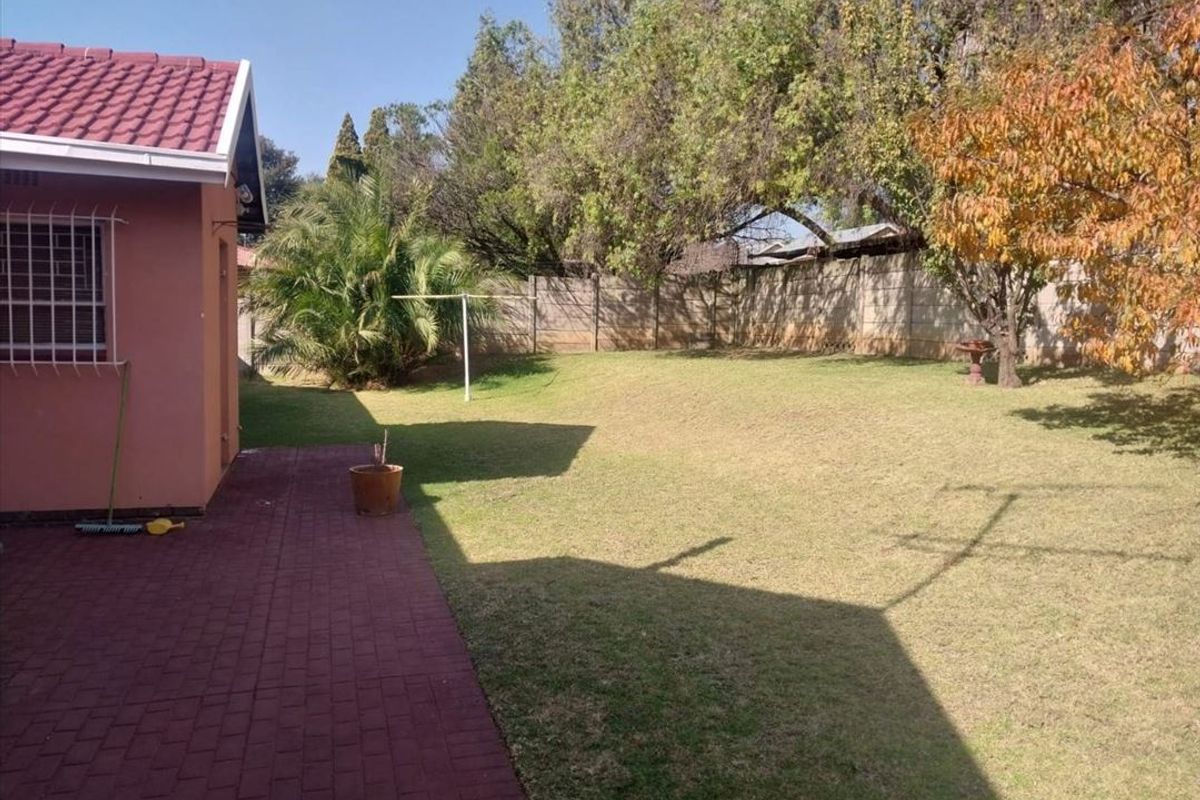 A spacious rear garden featuring a paved patio area, established lawn, and secure perimeter walling.