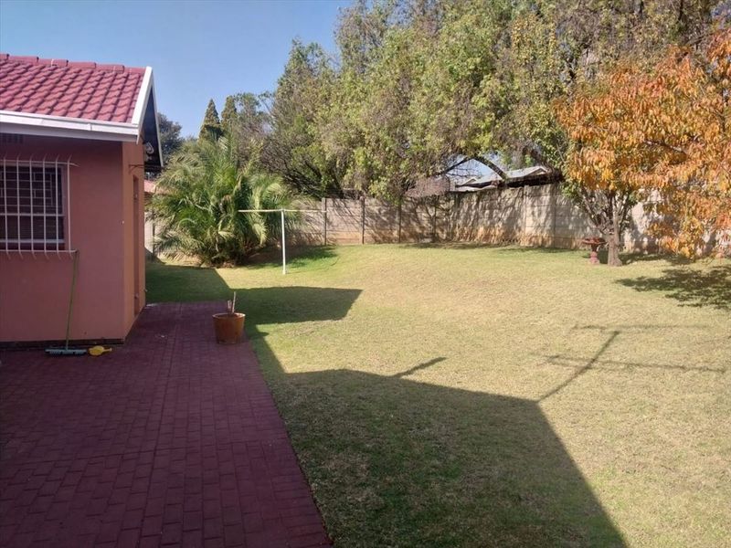 A spacious rear garden featuring a paved patio area, established lawn, and secure perimeter walling.