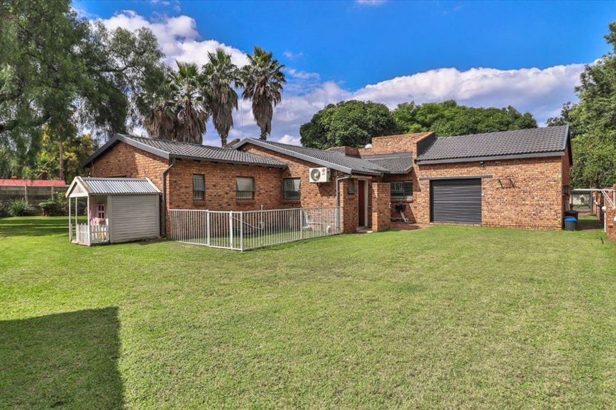 Rear view of the property featuring a spacious lawn, brick exterior walls, a garage with a roller door, and a fenced-off area.