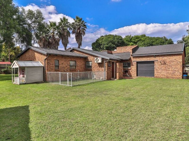 Rear view of the property featuring a spacious lawn, brick exterior walls, a garage with a roller door, and a fenced-off area.