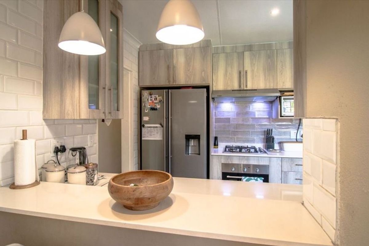 Modern kitchen featuring light wood-grain cabinetry, subway tile backsplash, stone countertops, and integrated stainless steel appliances including an oven and extractor fan.