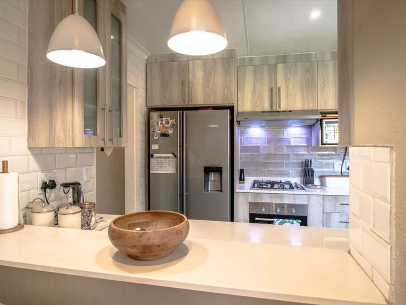 Modern kitchen featuring light wood-grain cabinetry, subway tile backsplash, stone countertops, and integrated stainless steel appliances including an oven and extractor fan.