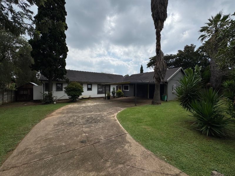 Front view of a single-story residential property featuring a concrete driveway, attached carport, and established garden surroundings.