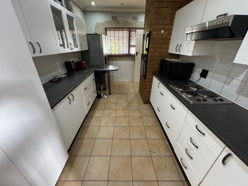 A functional kitchen featuring white cabinetry, dark countertops, an electric hob, and an exposed brick feature wall, requiring some cosmetic finishing and floor repairs.