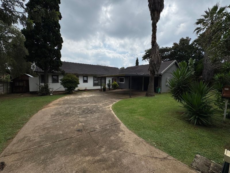 Front exterior view of a single-story house featuring a concrete driveway, carport, and established garden area.