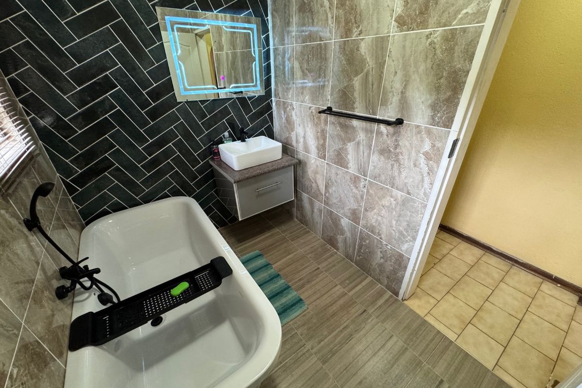 Modern bathroom featuring a freestanding bathtub, wall-mounted vanity with vessel sink, LED mirror, and stylish herringbone wall tiling with matte black fixtures.