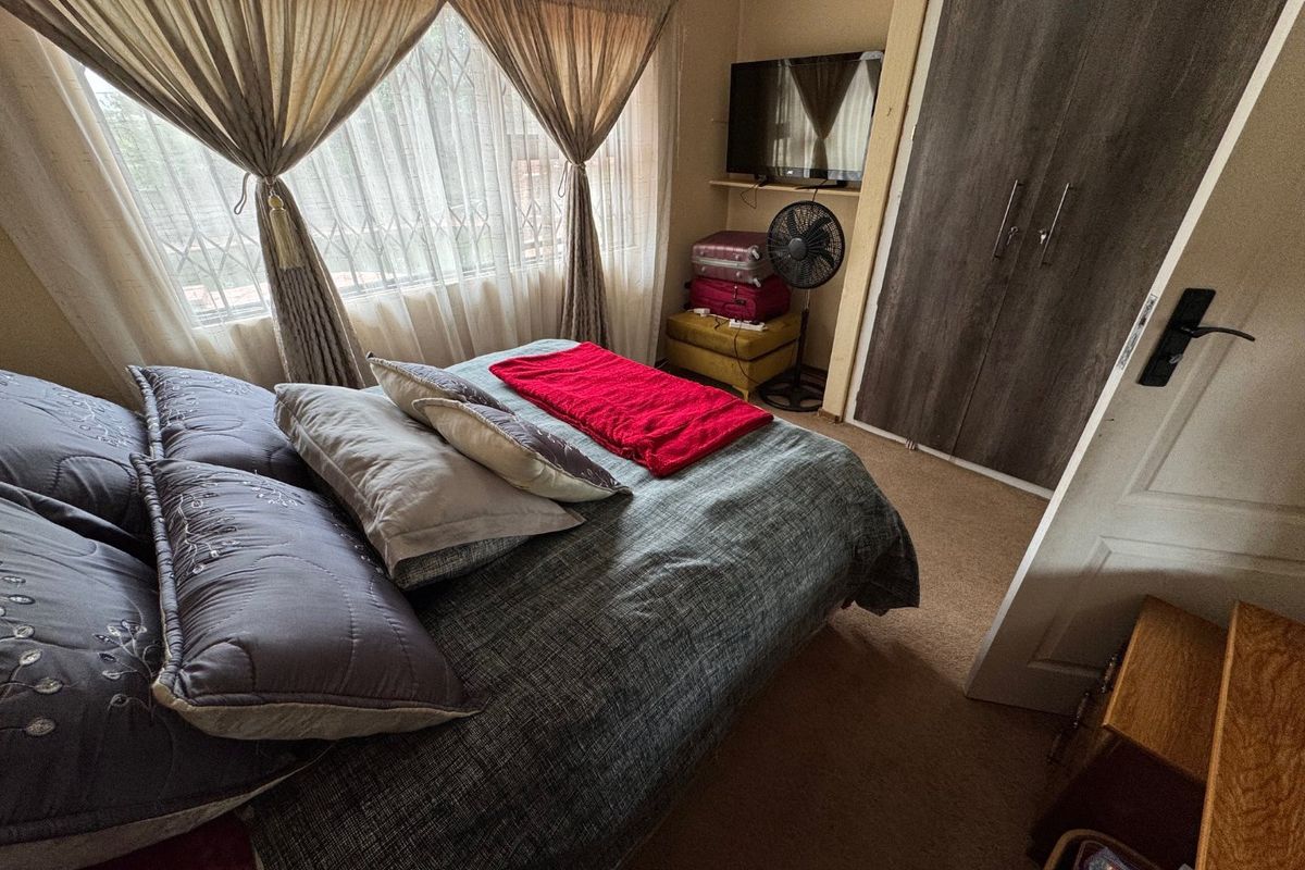 A functional bedroom featuring a built-in wardrobe, carpeted flooring, and a window fitted with a security gate.