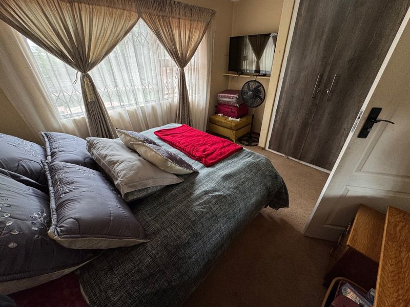 A functional bedroom featuring a built-in wardrobe, carpeted flooring, and a window fitted with a security gate.