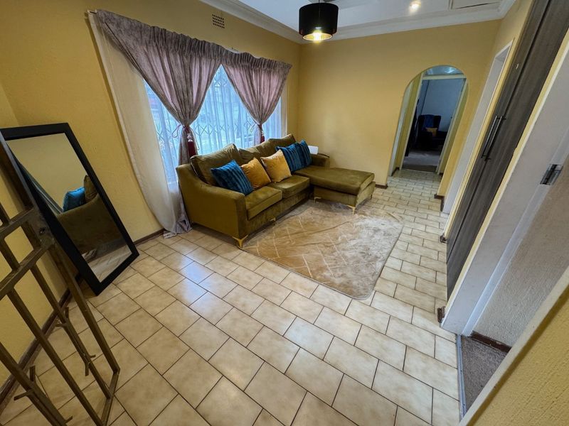 A living room featuring tiled flooring, an arched doorway, and security bars on the window, providing a functional space with potential for modern updates.