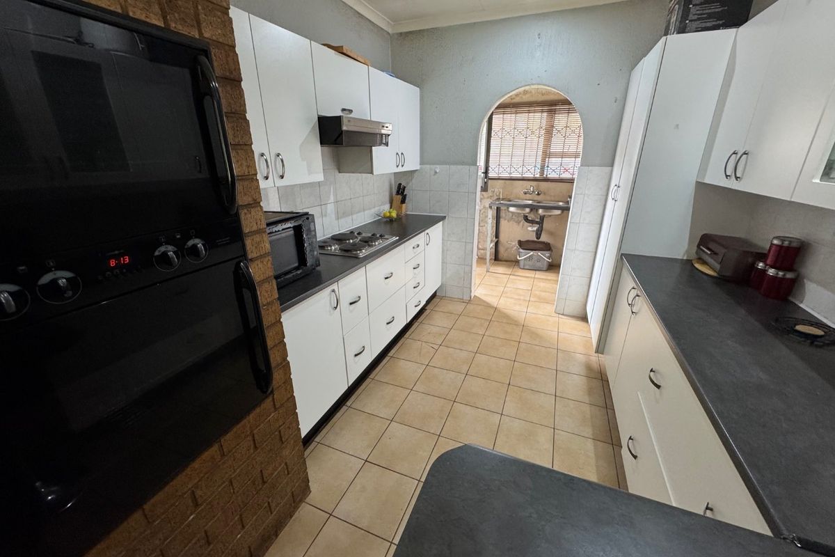 A functional kitchen featuring white cabinetry, dark countertops, built-in oven, and hob, with an adjoining scullery area accessed through a classic archway.