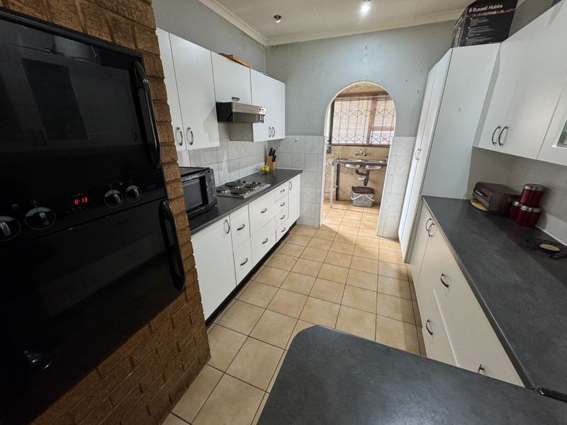 A functional kitchen featuring white cabinetry, dark countertops, built-in oven, and hob, with an adjoining scullery area accessed through a classic archway.
