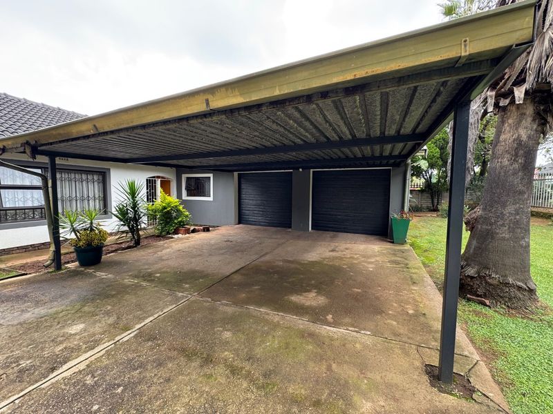 A double garage with a covered carport area and concrete driveway, providing ample off-street parking space.