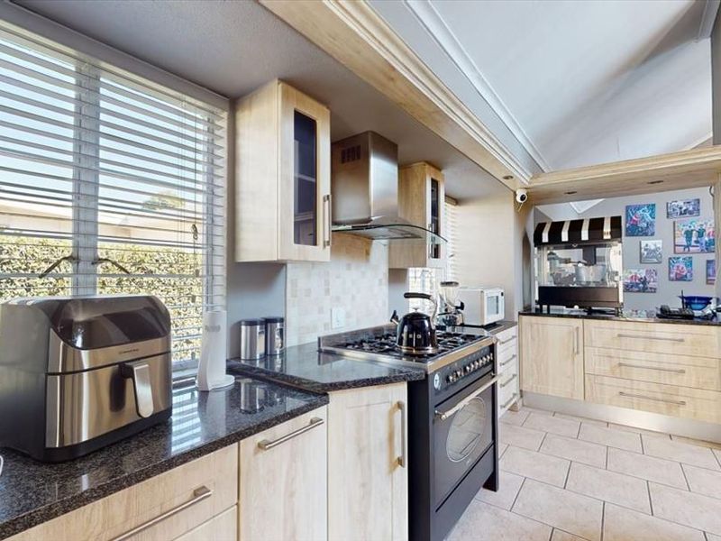 A well-lit kitchen featuring light wood cabinetry, granite countertops, a gas stove with extractor fan, and tiled flooring.
