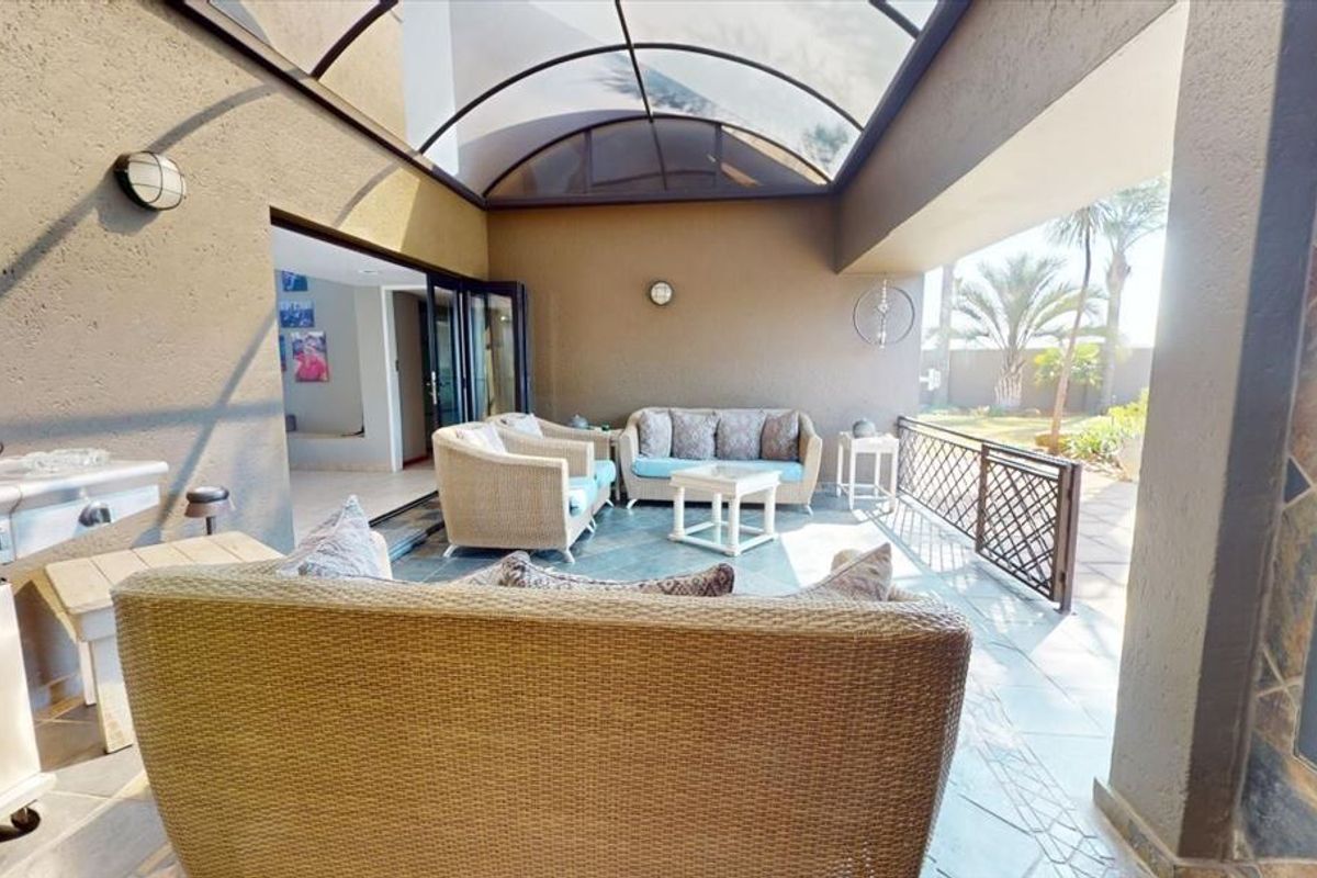 Covered patio featuring a built-in braai, arched roof structure, and tiled flooring, providing a seamless transition to the garden area.
