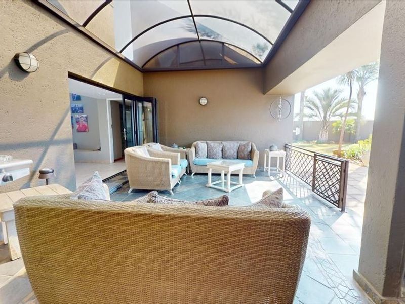 Covered patio featuring a built-in braai, arched roof structure, and tiled flooring, providing a seamless transition to the garden area.