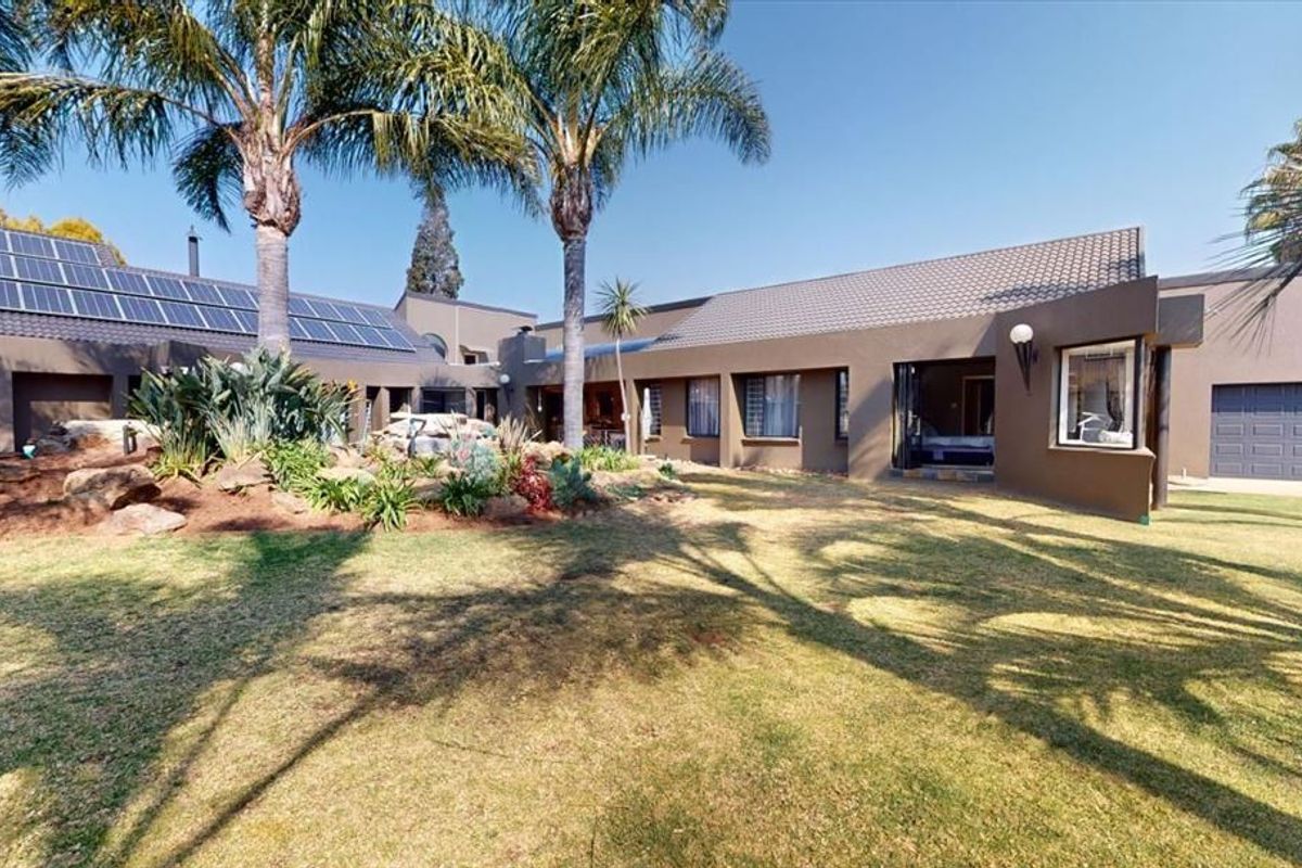 Spacious rear exterior view featuring a well-maintained garden, rockery, and solar panel installation on the tiled roof.