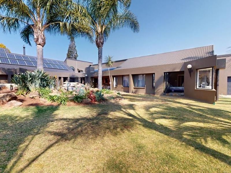 Spacious rear exterior view featuring a well-maintained garden, rockery, and solar panel installation on the tiled roof.
