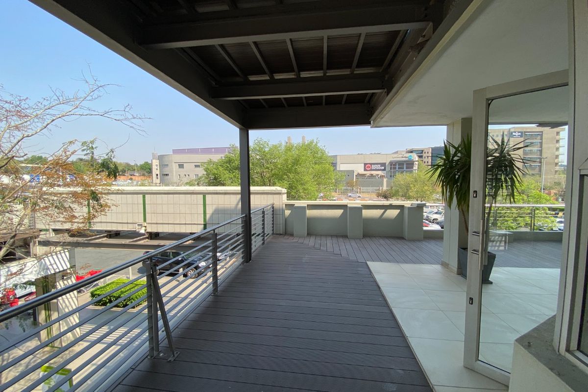 A spacious covered balcony featuring timber decking, a modern stainless steel balustrade, and direct access to the interior through a glass door.
