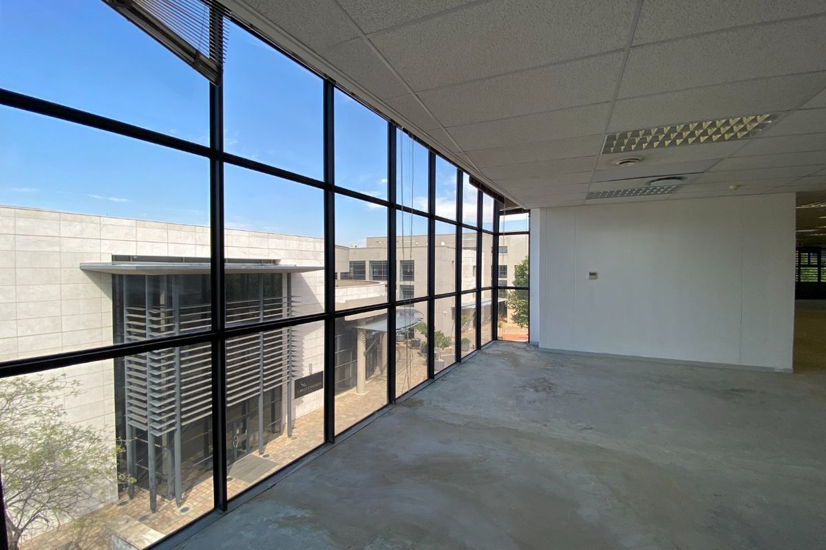 Empty commercial office space featuring floor-to-ceiling windows with views of the surrounding business park and suspended ceiling grid.