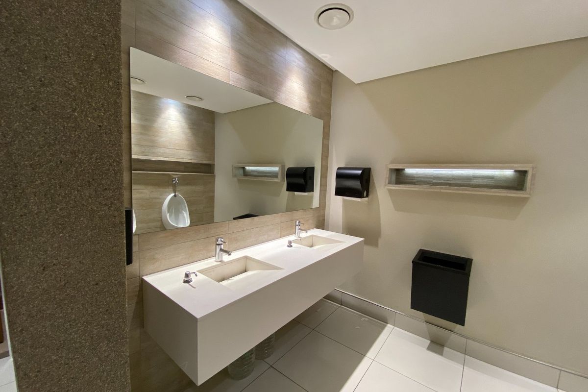 Modern commercial bathroom featuring a sleek double vanity with wall-mounted faucets, large mirror, and contemporary tiled finishes.