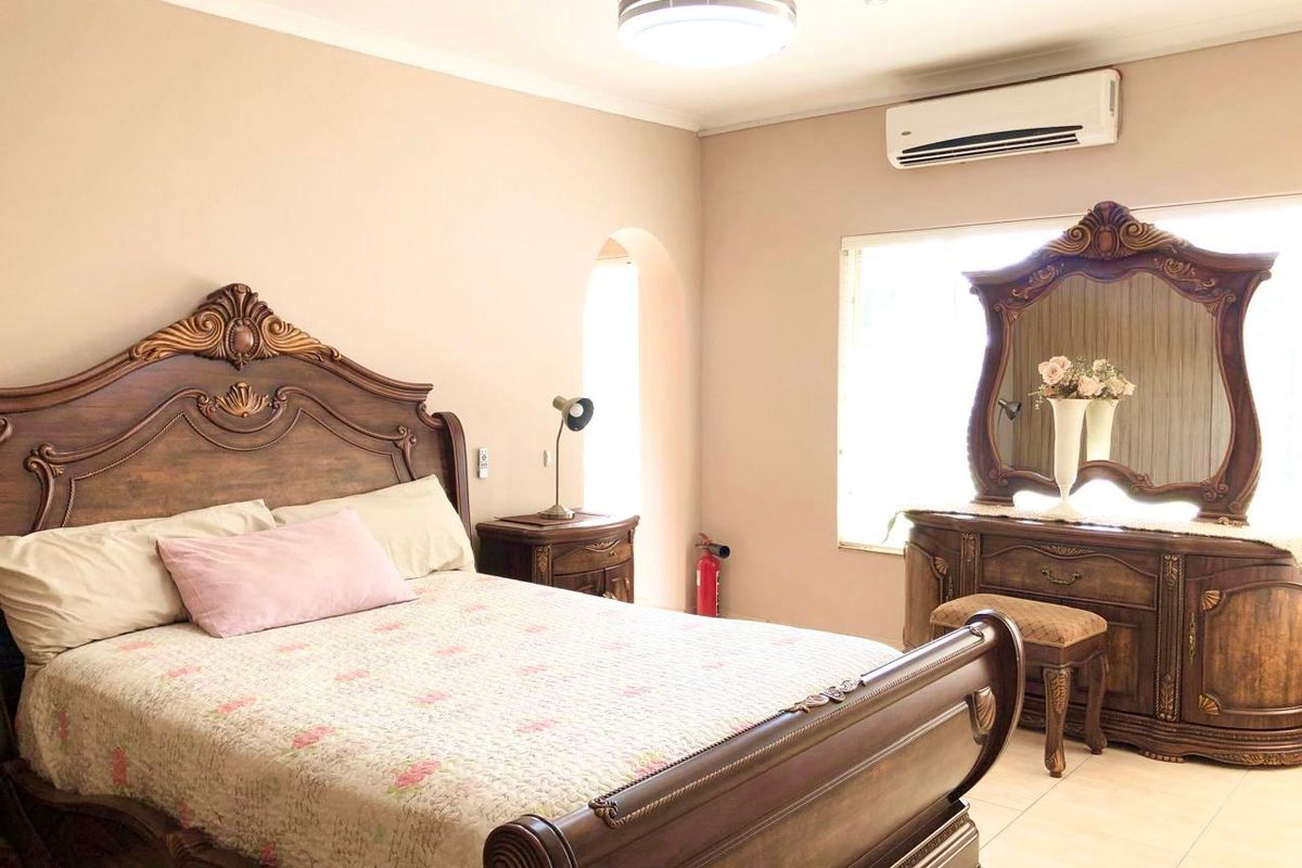 A spacious bedroom featuring tiled flooring, a ceiling fan, and a wall-mounted split-system air conditioner.
