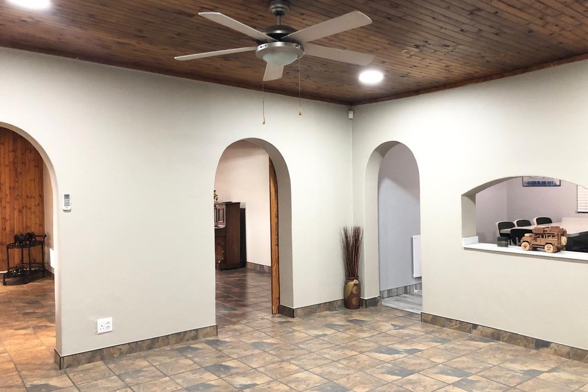 Spacious living area featuring a timber-clad ceiling, arched doorways, and tiled flooring, offering a versatile layout with a convenient serving hatch to the kitchen.