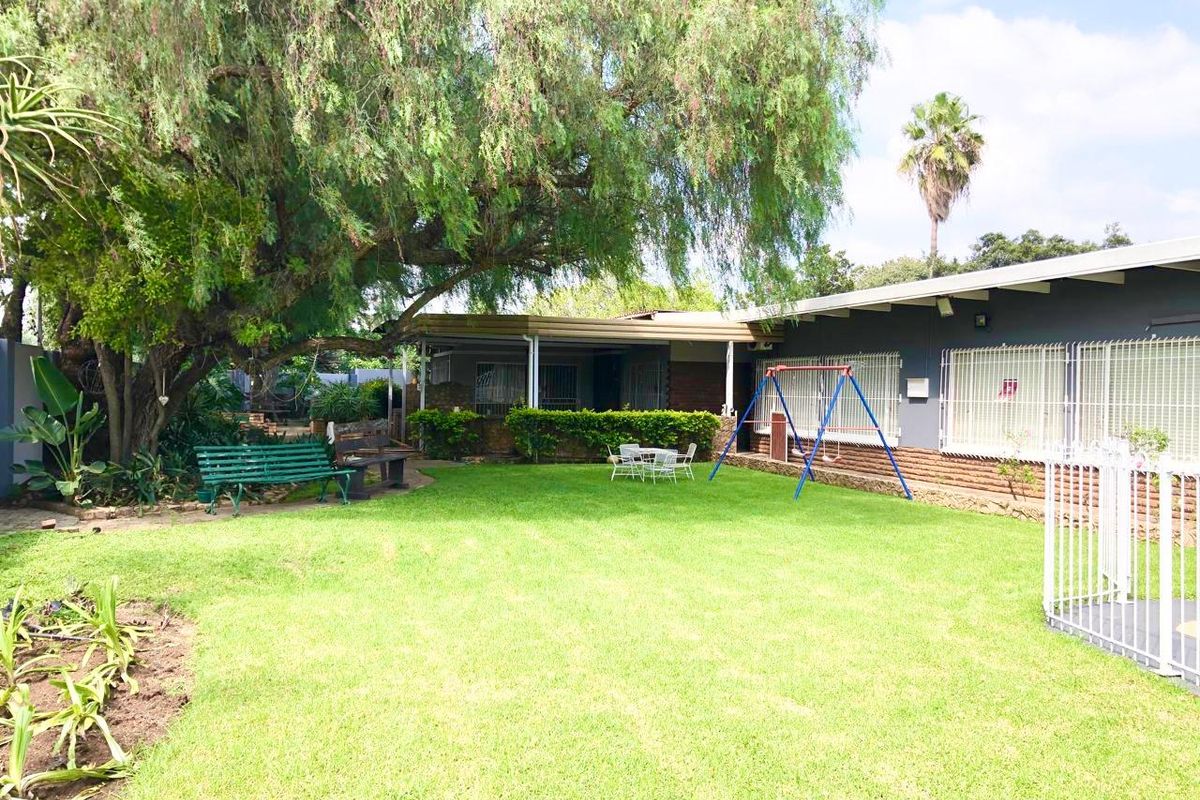 A spacious rear garden featuring a well-maintained lawn, mature trees, and a covered patio area attached to the main house structure.