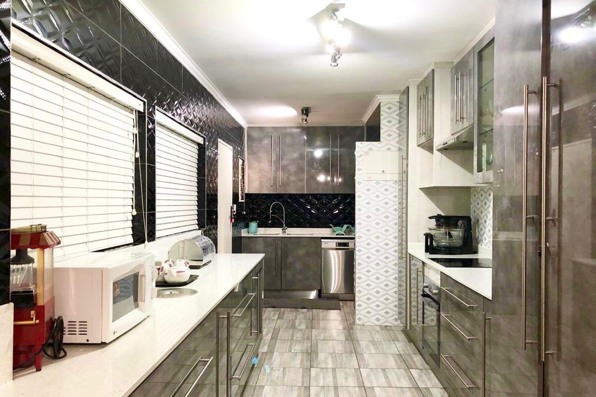 Modern galley-style kitchen featuring high-gloss cabinetry, stone countertops, integrated appliances, and a striking black tiled backsplash.
