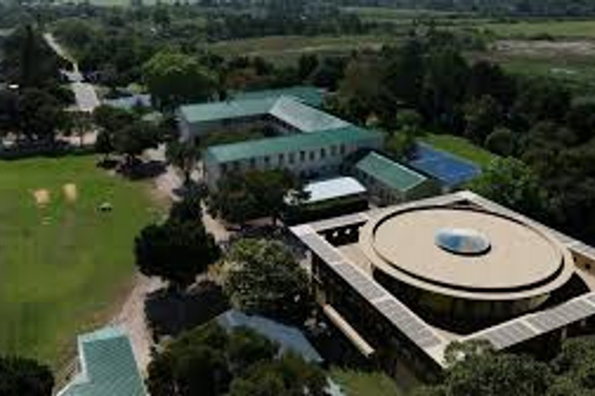 Aerial view of a large property complex featuring multiple buildings, including a distinctive circular structure with a central skylight, set within expansive green grounds.
