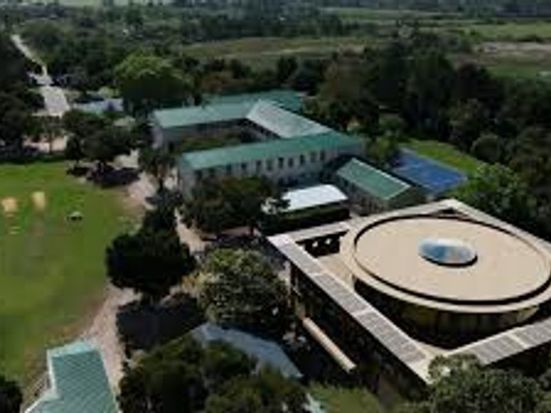 Aerial view of a large property complex featuring multiple buildings, including a distinctive circular structure with a central skylight, set within expansive green grounds.