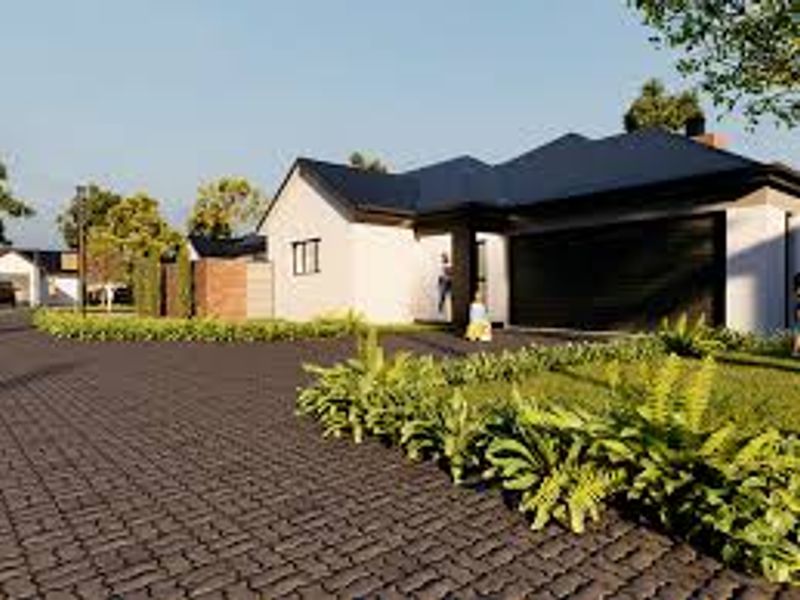 A modern residential property exterior featuring a paved driveway, landscaped garden, and a clean, contemporary facade with a pitched roof.