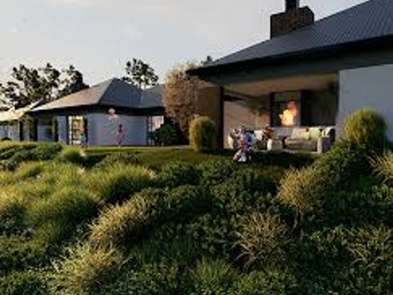 A rear view of a modern house featuring a covered patio area, brick chimney, and extensive landscaped garden.