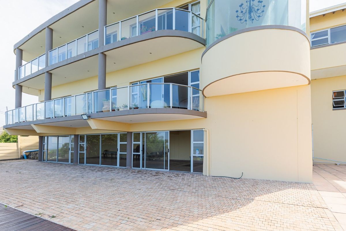 Rear elevation of a multi-story property featuring extensive glass balustrades, sliding doors, and a spacious paved patio area.